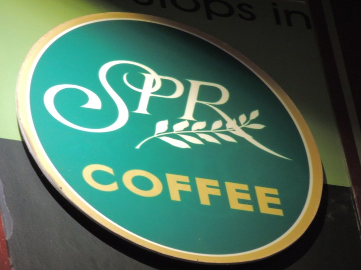 Large, round sign that reads S P R Coffee against a green background.