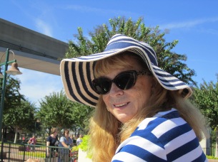 My wife Sandy wearing a soft blue and white striped hat with a large, floppy brim. She has on a matching top, dark sunglasses, and long, light colored hair.